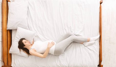 Pregnant woman lifestyle and health care. Young expectant lady napping in bed, top view with empty space
